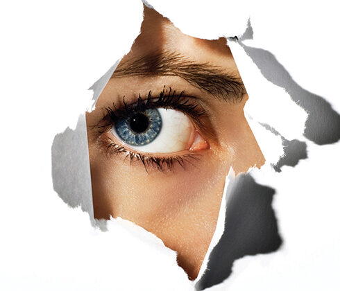 an eye peeking throw a hole in the paper